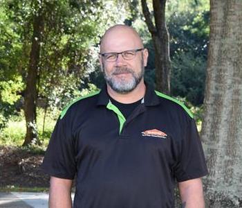 Male employee in black shirt with trees in background